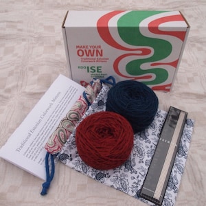 Pu&ograve; includere: Un kit per realizzare i tuoi guanti tradizionali estoni in colorwork. Il kit include due gomitoli di lana, uno rosso e uno blu, un set di ferri da maglia e una borsa di stoffa con motivo paisley. La scatola ha un design a spirale verde e rosso e il testo "Make Your Own Traditional Estonian Colorwork Mittens" sul davanti.