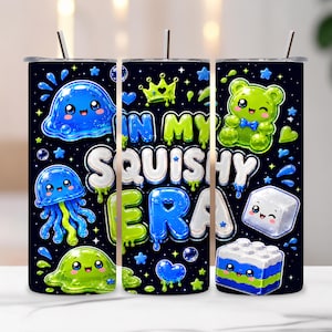 May include: A cylindrical tumbler with a black background featuring a colorful pattern of cartoon characters including a blue jellyfish, green slime, a gummy bear, and a building block. The text "IN MY SQUISHY ERA" is printed in large, bubbly letters.