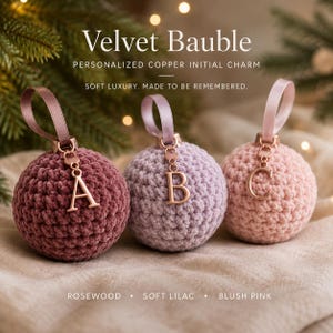 May include: Three round crochet baubles in rosewood, soft lilac, and blush pink. Each bauble features a satin ribbon loop and a copper-colored metal initial charm hanging from the top. The text reads Velvet Bauble, Personalized Copper Initial Charm, Soft Luxury. Made to be remembered. Rosewood, Soft Lilac, Blush Pink.