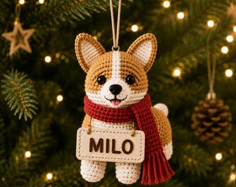May include: A crocheted Corgi ornament featuring tan and white yarn, black eyes, and a small pink tongue. The dog wears a textured red scarf and holds a rectangular beige sign with the name MILO in dark brown letters, suspended by a string.