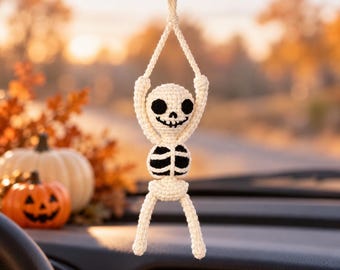 May include: A crocheted skeleton car accessory hanging from a rearview mirror. The figure is made of off-white yarn with black yarn details for the eye sockets, nose, and rib cage. It features a loop at the top for hanging and articulated limbs.