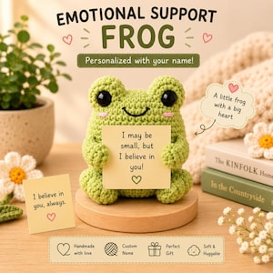 May include: A light green crocheted frog plush toy with large black eyes and pink cheeks, holding a yellow square note that reads, I may be small, but I believe in you! The frog sits on a round wooden base, surrounded by text and decorative elements.