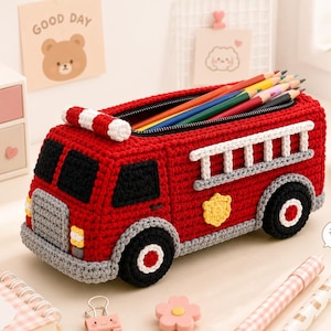 May include: A red crochet pencil case shaped like a fire truck with black windows, a grey bumper, white ladder details on the side, and black wheels with red centers. The top is open, revealing several colored pencils stored inside the main compartment.