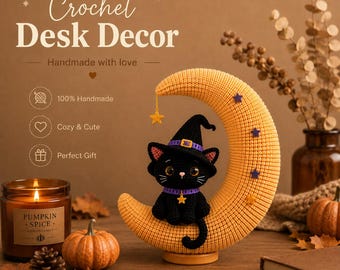 May include: A crocheted black cat wearing a purple-trimmed witch hat and collar with a star charm, sitting on a large, textured orange crescent moon. The moon is decorated with small purple and yellow stars, and a yellow star hangs from the tip.