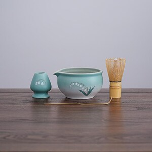 Puede incluir: Un juego de té matcha con un cuenco de cerámica azul claro, un batidor y un soporte. El juego incluye un batidor y una cuchara de bambú. Cada pieza está decorada con un diseño de lirio de los valles.