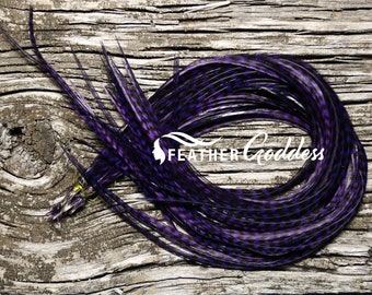 Può includere: Un mazzo di piume viola e nere con un logo bianco "FEATHER GODDESS". Le piume sono disposte in cerchio su una superficie di legno.
