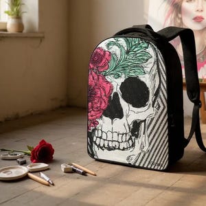 Puede incluir: Mochila negra con diseño de calavera con rosas rosas y hojas verdes. La calavera tiene una cuenca del ojo negra y un patrón de rayas blancas y negras. La mochila tiene correas negras.