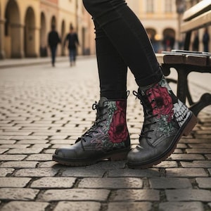 Puede incluir: Botas de combate grises con un diseño floral y de calavera. Las botas tienen cierre de cordones y suela marrón oscuro. El diseño floral incluye grandes rosas rojas y hojas verdes. Las botas se llevan con pantalones negros.