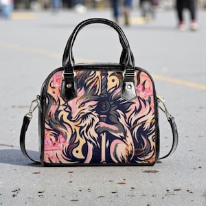 Può includere: Borsa a mano nera e rosa con un disegno di lupo. La borsa ha un manico nero e una tracolla staccabile. Il disegno del lupo è nei toni del rosa, beige e nero. La borsa è su una superficie grigia.