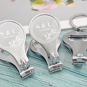 Könnte beinhalten: Silberne Nagelknipser mit einem runden Oberteil, das mit den Initialen "S & L" und dem Datum "16.8.2025" graviert ist. Die Knipser haben ein Blumendesign und sind an einem Schlüsselring befestigt. Ein Knipser hat einen Flaschenöffner.