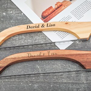 May include: Two wooden bread slicers with stainless steel blades. The top slicer is light-colored wood, and the bottom is a darker wood. Both are engraved with "David & Lisa". The slicers are on a gray surface.