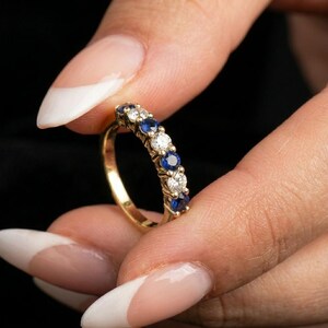 May include: A yellow gold band ring featuring an alternating row of round-cut blue sapphires and clear white diamonds. The stones are set in a prong setting along the top half of the band, creating a continuous sparkling display of blue and white.