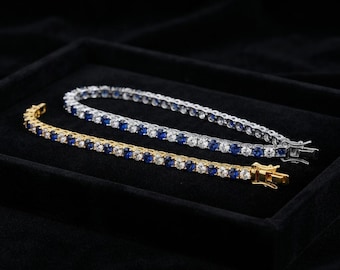 May include: Two tennis bracelets featuring alternating round-cut blue sapphire and clear white stones. One bracelet is set in a polished yellow gold-tone metal, while the other is set in a polished silver-tone metal, both with secure box clasps.