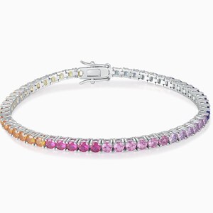 May include: A silver-toned tennis bracelet featuring a continuous row of round-cut gemstones in a vibrant gradient color scheme, transitioning from orange and red to various shades of pink and purple, secured with a metal box clasp closure.