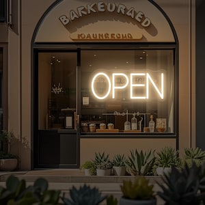 May include: Exterior shot of a shop with a glowing neon "OPEN" sign in the window. The shop's name is displayed above the window. Potted plants line the entrance. The shop appears to be a cafe or restaurant.