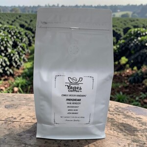 May include: A white bag of Yanes Coffee Co. whole bean coffee. The bag features the text "PARAINEMA 100% ARABICA MEDIUM ROAST WHOLE BEAN USDA ORGANIC." The net weight is 450g (1 lb). The background shows a coffee plantation.