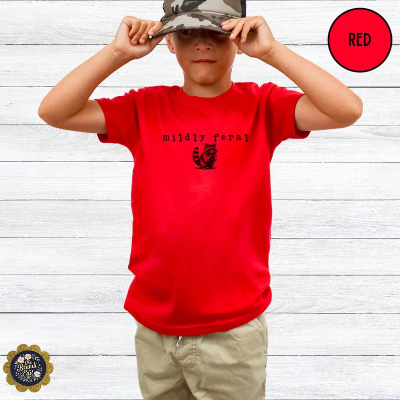 Puede incluir: Una camiseta roja de manga corta con un gr&aacute;fico negro de un mapache y el texto "mildly feral" impreso en una fuente estilo m&aacute;quina de escribir en el pecho. La camiseta tiene cuello redondo y un corte est&aacute;ndar en un color s&oacute;lido.
