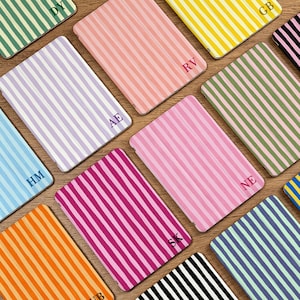 May include: A collection of colorful, striped tablet cases in various shades, including pink, green, yellow, and blue. Each case features a unique initial in the corner. The cases are arranged on a wooden surface.