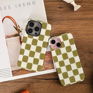 Peut inclure: Deux coques de téléphone avec un motif à carreaux vert et blanc. Les coques sont posées sur un magazine avec le texte "LES IRENG". Elles sont sur une surface en bois.