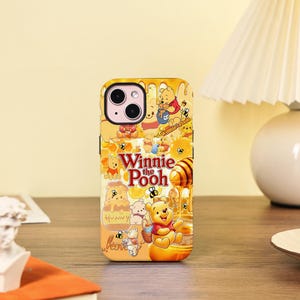 Peut inclure: Coque de téléphone jaune avec un motif Winnie l'Ourson, du miel et des abeilles. La coque porte l'inscription "Winnie the Pooh". Le design comprend des illustrations de Winnie l'Ourson et de pots de miel.
