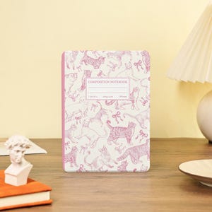 Könnte beinhalten: Ein Notizbuch mit einem rosa Katzenmuster. Das Notizbuch hat einen rosa Buchrücken und der Einband zeigt verschiedene Katzenillustrationen in Rosatönen. Der Text "COMPOSITION NOTEBOOK" ist auf dem Einband aufgedruckt. Das Notizbuch misst 19 x 25 cm.