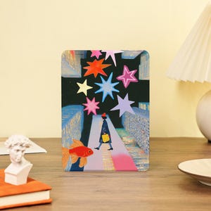 May include: A rectangular art print with a whimsical illustration. It shows a person walking on a city street at night, with colorful stars and a goldfish. The color palette includes black, blue, pink, orange, and yellow. The print is a decorative item.