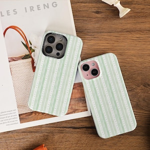 Może przedstawiać: Dwa etui na telefon z jasnozielonym i białym wzorem w paski. Etui mają pionowy wzór w paski z małymi kropkowanymi liniami między paskami. Etui na telefon leżą na drewnianej powierzchni.