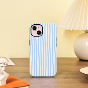 Può includere: Una custodia per smartphone con un motivo a righe blu e bianche. La custodia è progettata per adattarsi a uno smartphone e presenta un ritaglio per la fotocamera. La custodia è su una superficie di legno.