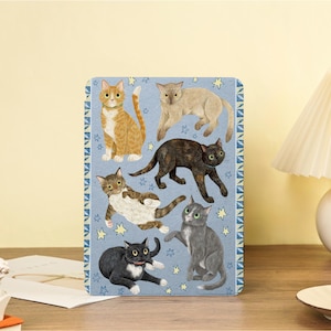 Peut inclure: Un objet décoratif rectangulaire bleu avec des illustrations de six chats dans différentes poses. Les chats sont dans des tons orange, marron, gris et noir. Le fond présente un motif d'étoiles.