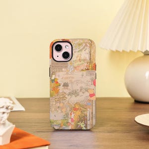 May include: A beige iPhone case with illustrations of Winnie the Pooh characters. The case has a vintage map design with text and images of the characters. The case is on a wooden surface.