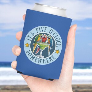 Op de afbeelding: Een blauwe schuimrubberen blikkoeler met een cirkelvormige afbeelding met de tekst IT'S FIVE O'CLOCK SOMEWHERE, twee kleurrijke papegaaien en een margaritaglas. Het ontwerp bevat twee gele sterren op een lichtblauwe achtergrond.