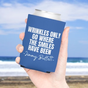 May include: A blue foam can cooler featuring the white printed text WRINKLES ONLY GO WHERE THE SMILES HAVE BEEN and the signature -Jimmy Buffett- in a script font. The beverage insulator is designed to fit a standard metal drink can.