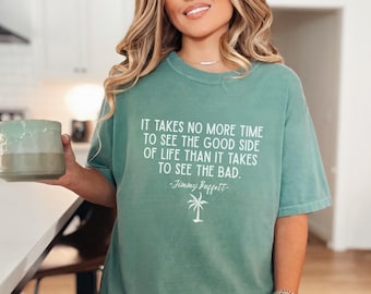 May include: A teal-colored t-shirt with the quote "IT TAKES NO MORE TIME TO SEE THE GOOD SIDE OF LIFE THAN IT TAKES TO SEE THE BAD." by Jimmy Buffett. The shirt also features a palm tree graphic.