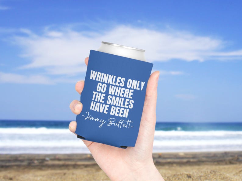 May include: A blue foam can cooler featuring the white printed text WRINKLES ONLY GO WHERE THE SMILES HAVE BEEN and the signature -Jimmy Buffett- in a script font. The beverage insulator is designed to fit a standard metal drink can.