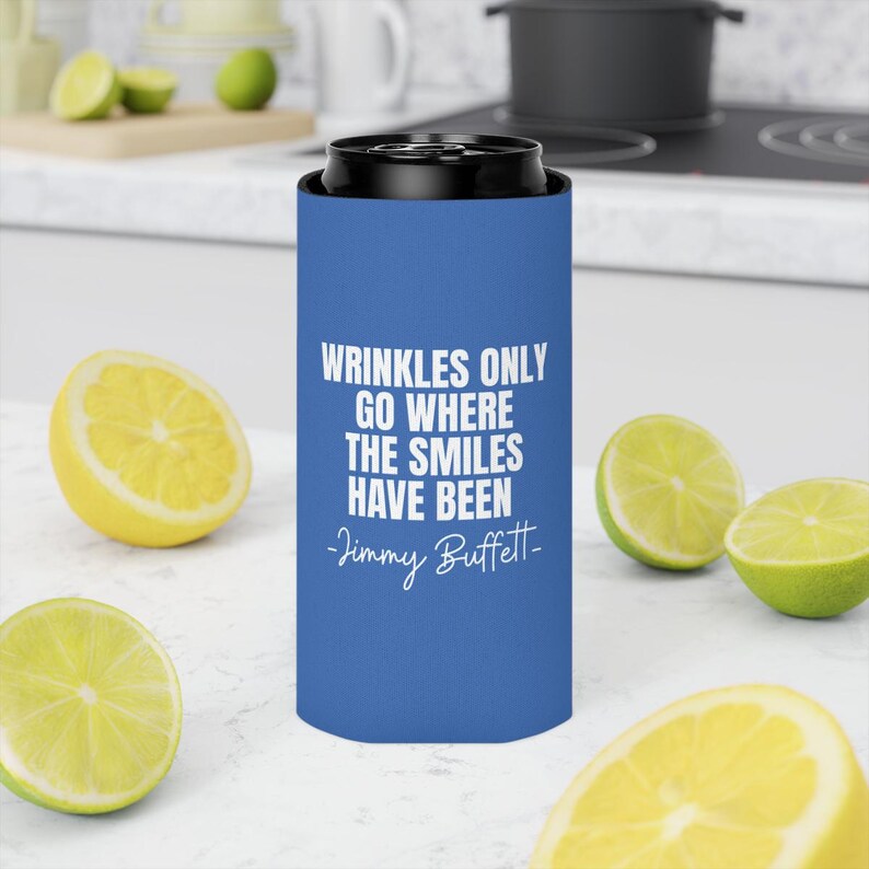 May include: A blue slim can cooler featuring the white printed text WRINKLES ONLY GO WHERE THE SMILES HAVE BEEN -Jimmy Buffett. The cylindrical beverage insulator has a black rim and is designed to hold a standard slim beverage can securely.