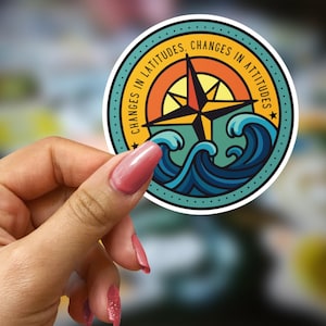 Pode incluir: Um autocolante redondo com um desenho de bússola, ondas e o texto "CHANGES IN LATITUDES, CHANGES IN ATTITUDES". A bússola apresenta um design de estrela vermelha e amarela. O autocolante tem uma borda turquesa com estrelas amarelas.