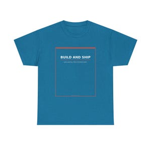 May include: A blue short-sleeve t-shirt featuring a rectangular orange outline on the chest. Inside the rectangle, the text reads BUILD AND SHIP in white, followed by the smaller white text Less wasting. More finished work. The shirt has a crew neck.