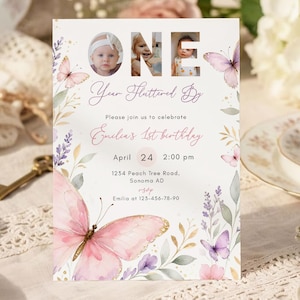 May include: A birthday invitation with a butterfly theme. The invitation features the word "ONE" with photos inside the letters. The text reads "Your Fluttered By" and "Emilia's 1st birthday". The invitation is decorated with watercolor butterflies and floral elements.