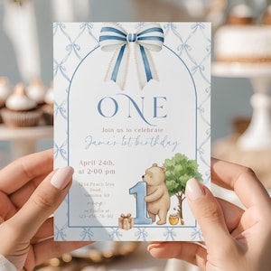 Può includere: Un biglietto d'invito per il compleanno tenuto in mano. La carta presenta un design a fiocco blu e bianco nella parte superiore, con la parola "ONE" al centro. Sotto, il testo recita "Unisciti a noi per festeggiare il 1° compleanno di James". Sono presenti anche un orso e un albero dei cartoni animati.