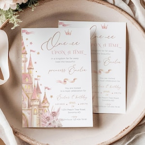 以下が含まれることがあります： ピンクの城のイラストと「Once Upon a Time」のテキストが入った、プリンセスをテーマにした2枚の招待状。カードは、誕生日のパーティーに最適な、花柄と布のアクセントが付いた装飾的なお皿の上にあります。