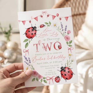 May include: A white invitation card with a ladybug theme. The card features the text "Our Little Lady is turning TWO" with floral and ladybug illustrations. The invitation includes details for a second birthday celebration.