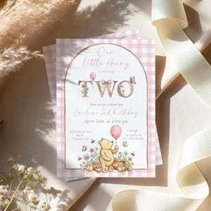 Puede incluir: Una invitaci&oacute;n de cumplea&ntilde;os para dos a&ntilde;os con un fondo de cuadros rosas. La invitaci&oacute;n incluye el texto "Our Little Hunny is turning TWO" con detalles florales y mariposas. Una ilustraci&oacute;n de Winnie the Pooh sostiene un globo.