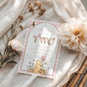 Puede incluir: Una invitaci&oacute;n de cumplea&ntilde;os para un ni&ntilde;o de dos a&ntilde;os, con un borde rosa a cuadros. El texto dice "Our Little Hunny is turning TWO" con detalles florales y mariposas. Incluye una ilustraci&oacute;n de Winnie the Pooh con un globo rosa.
