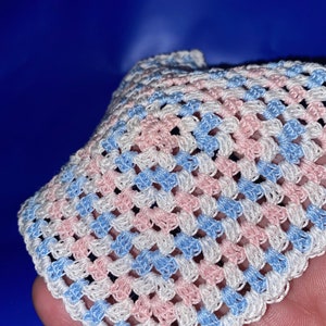 May include: A crocheted square with a white background and alternating blue and pink stripes.