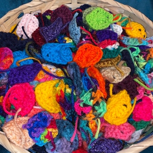 May include: A wicker basket overflowing with colorful crocheted circles and squares. The crocheted pieces are made in a variety of colors, including pink, purple, blue, green, yellow, orange, and red.