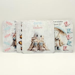 May include: A set of square coasters featuring a ghost character wearing boots and a blanket, with the text CUTE & CREEPY. The design includes illustrations of pumpkins, candies, and various coloured wellies on a light grey background.