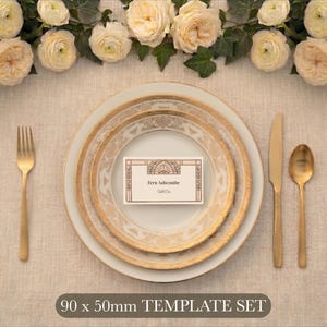 May include: A white place setting with gold-rimmed plates, a gold fork, knife, and spoon, and a rectangular place card reading Fern Ashcombe Table One. The card features a geometric design and measures 90 x 50 mm as indicated by the text.