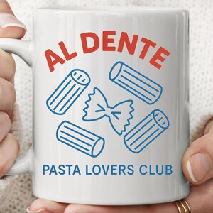 May include: White ceramic mug with the words "AL DENTE" in red and "PASTA LOVERS CLUB" in blue. The mug features blue line drawings of pasta shapes, including rigatoni and farfalle.