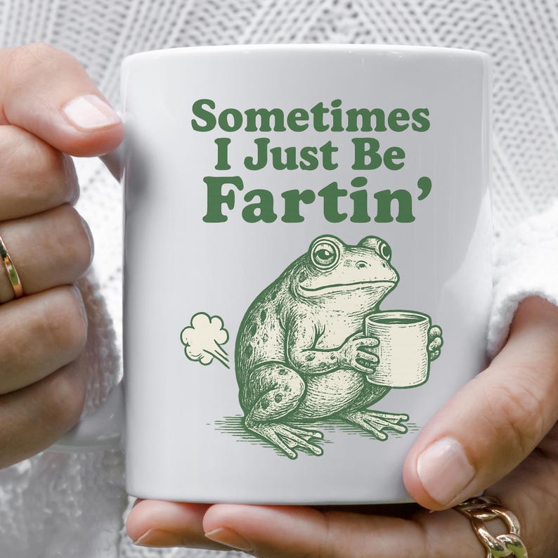 May include: White ceramic mug featuring a green frog holding a cup, with the phrase "Sometimes I Just Be Fartin'" in green lettering. The frog illustration includes a puff of gas. A humorous gift.