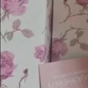 May include: A box and a brochure with a floral rose pattern in pink and white. The brochure features images of women in white dresses. The box is open, revealing the interior.